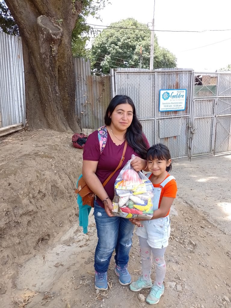 A mother and her daughter receive a donation of essential food supplies, a heartfelt gesture of kindness that supports their family
